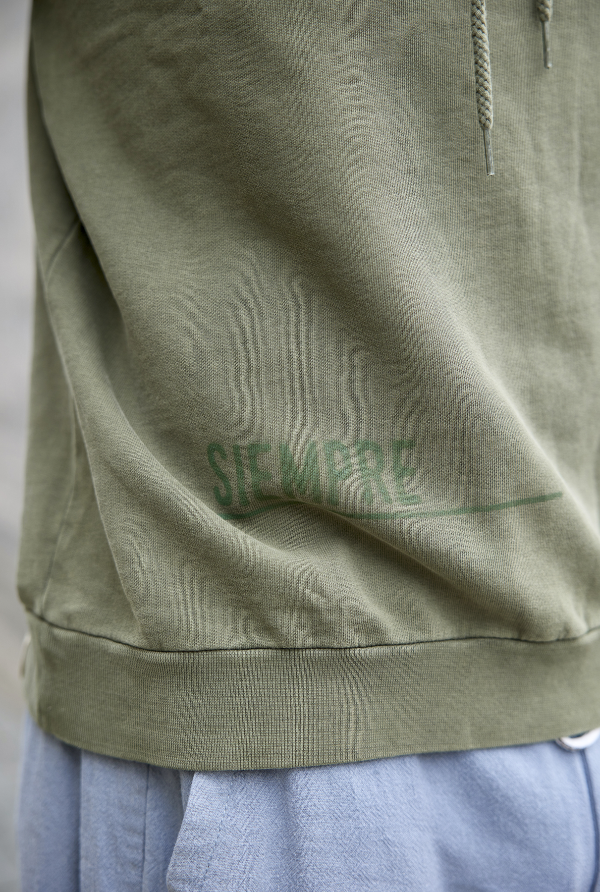 Polerón Millex Verde Oliva con cuello doble alto y capucha ajustable. Diseño en el frente que dice "caer levantarse siempre" en secciones. Fabricado con algodón de calidad.