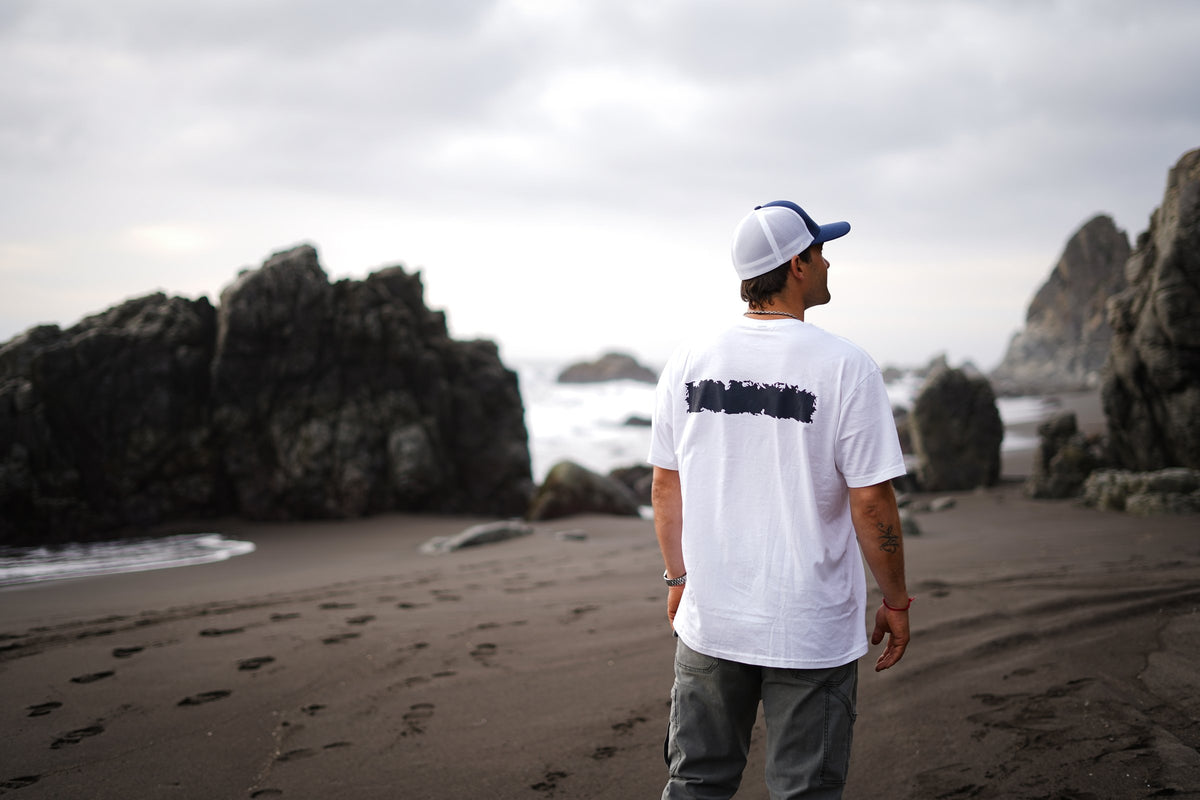 Polera Cicatriz blanca de COA de espaldas frente al mar